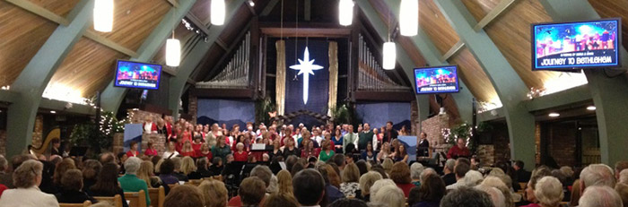 A church with a full audience watching and listening to a choir in front of the church.