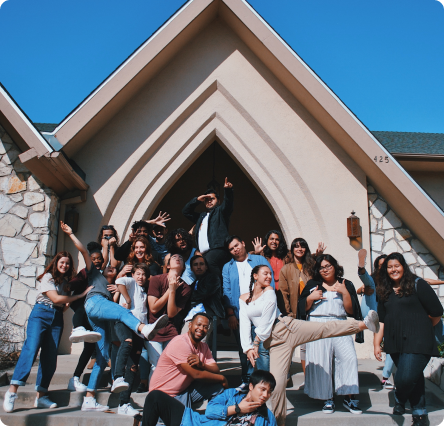 A group of teenagers posing in fun ways for a photo outside a church