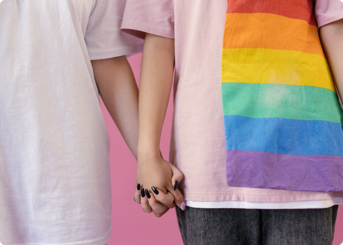 Two woman holding hands, one of them are wearing a shirt with the pride flag colors