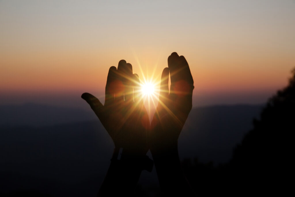 Spiritual prayer hands over sun shine with blurred beautiful sunset background